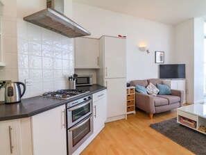A compact kitchen with modern appliances, a sofa, and a TV in a living area. - 4 Oceanside Apartments, Ilfracombe (Ilfracombe)