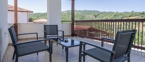 A balcony with a table and chairs, a view of a hilly landscape, and a wooden ceiling.