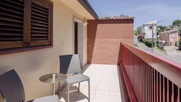 Un balcone con ringhiera rossa, due sedie e un tavolino.