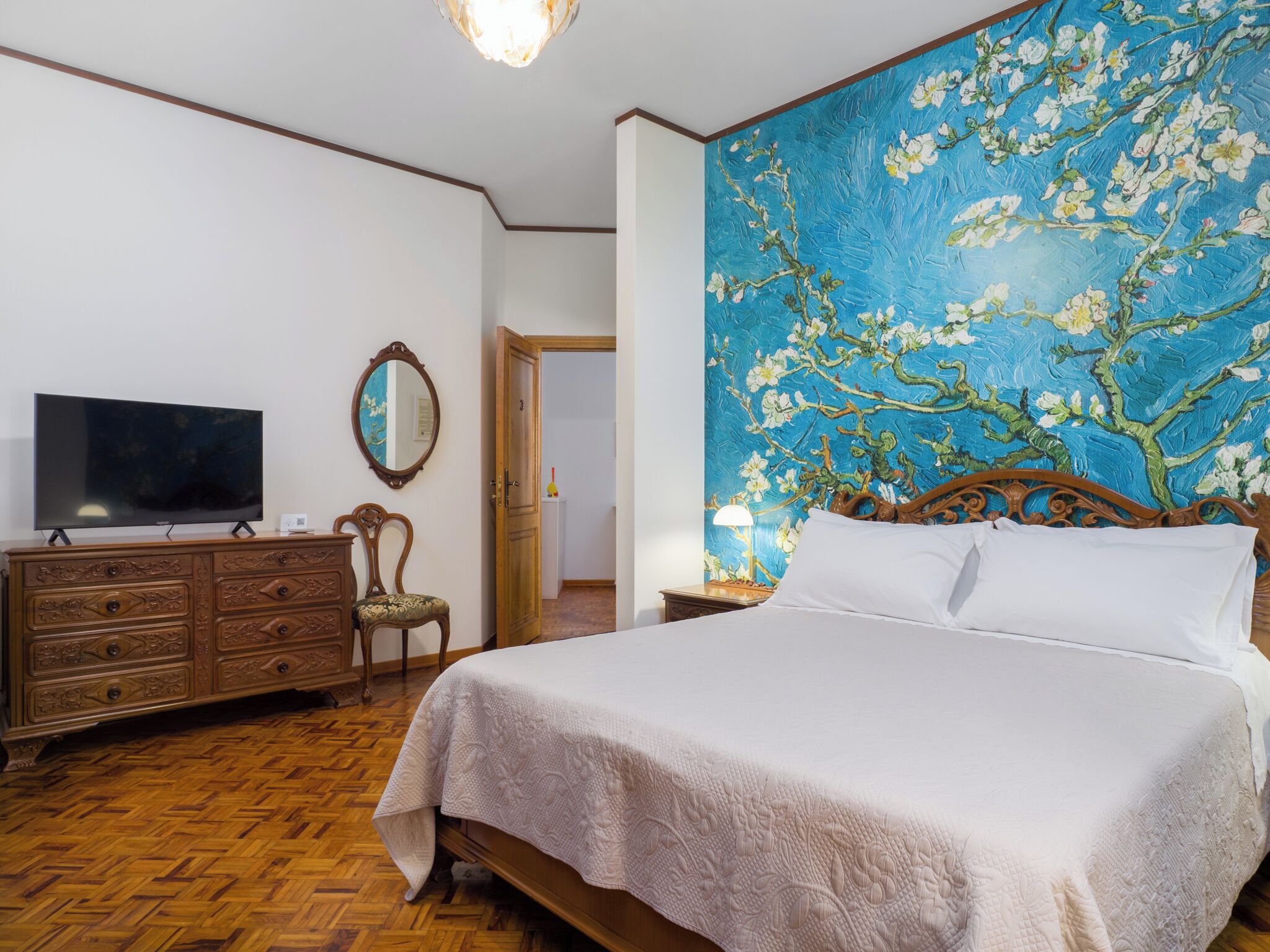 Une chambre à coucher avec un grand lit, une commode en bois, une télévision, un miroir et un tableau mural.