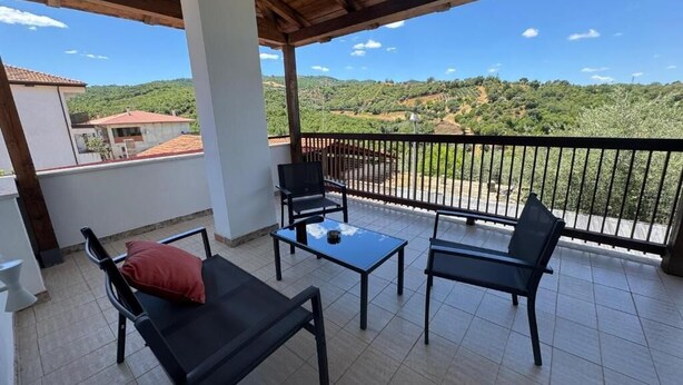A balcony with a view of a hilly landscape, a table, two chairs, and a sofa. - Ad Ricezioni Villa Francesca (San Demetrio Corone)