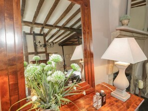 Ein spiegel mit Holzrahmen, der einen Raum mit einem Chandelier, einer weißen Lampe und einer Blumenvase reflektiert.