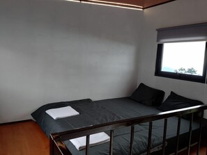Een eenpersoonsbed met metalen frame, een raam met uitzicht en een plafondlamp.