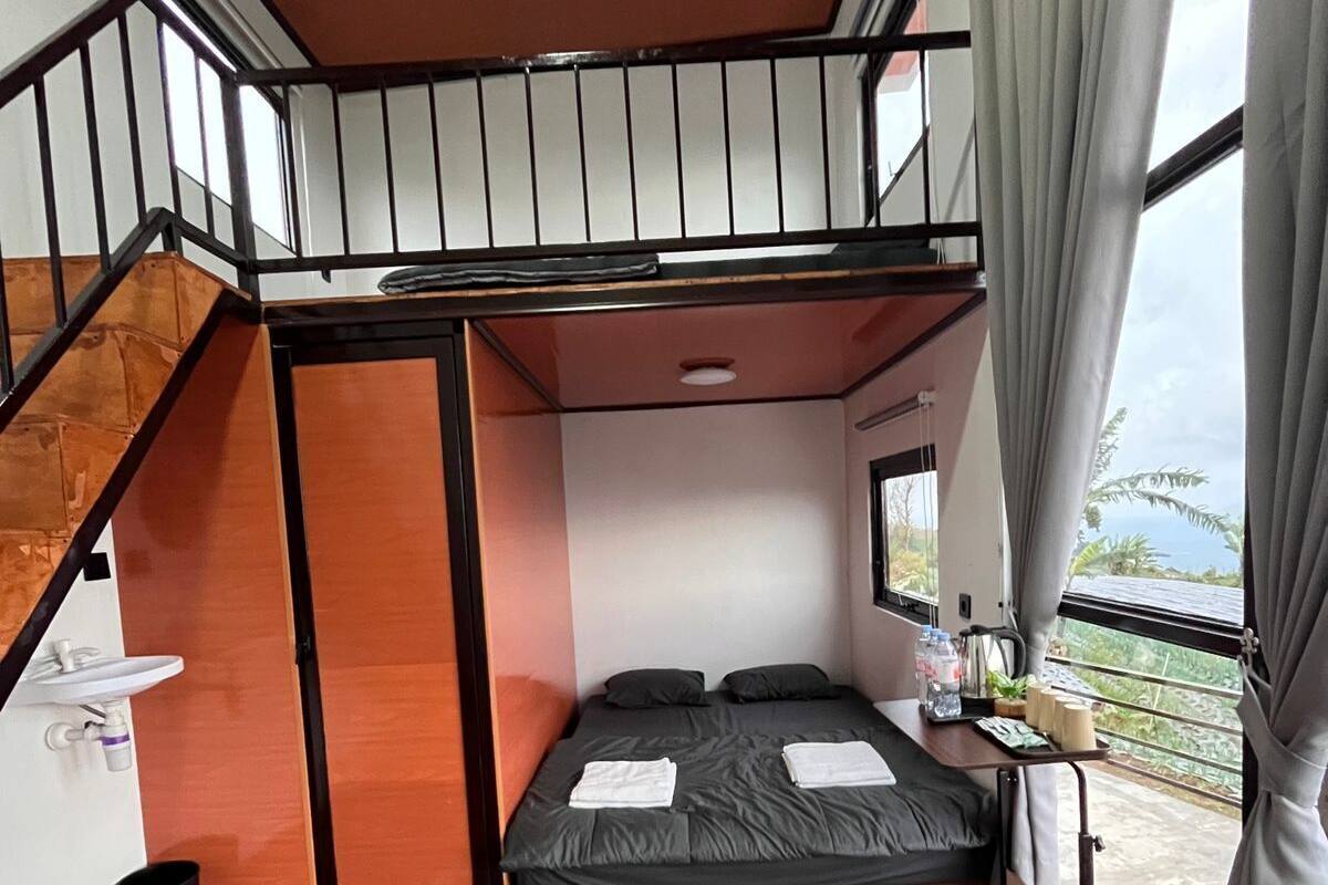 Une pièce de taille modeste, comprenant un lit superposé, un petit bureau avec une chaise, une fenêtre avec des rideaux et un plancher en bois.