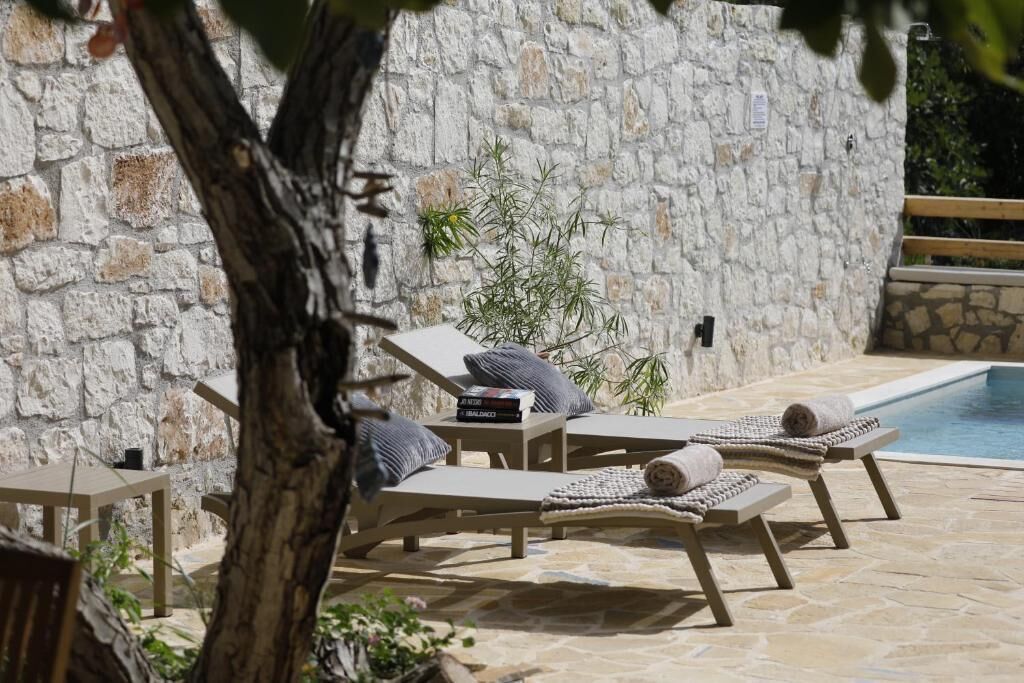 Un muro di pietra, una piscina e poltrone da relax con asciugamani e cuscini.