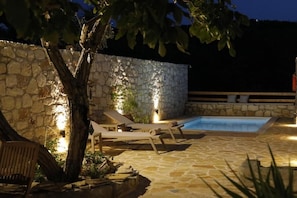 A stone pool with lounge chairs and a tree, surrounded by stone walls and outdoor lighting. - Ontas by Praxithea Traditional Home  (Apokoronas)