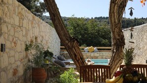 Eine Steinsäule, Holzmöbel, ein Pool und eine Anordnung tropischer Früchte.