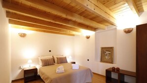 Ein Schlafzimmer mit Holzboden, einem Bett mit Kissen, einem Nachttisch mit Lampe, einem gerahmten Bild an der Wand und einem kleinen Holztisch mit Dekoration.