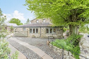 A stone building with a cobblestone pathway, a tree, and a wooden fence.