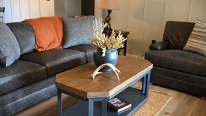 A modern living room with a dark leather sofa, a wooden coffee table with a vase of dried plants, and a lamp on a side table.