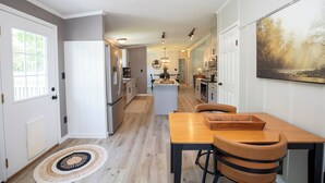 A modern kitchen with a central island, a dining area with a wooden table and chairs, and a hallway leading to a living space.
