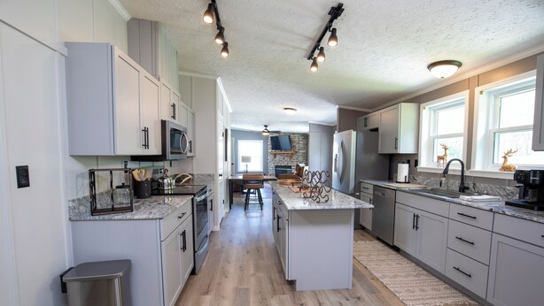 A modern kitchen with white cabinets, a central island, and a stone fireplace.