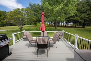 A deck with a grill, a table, and chairs, surrounded by a white railing and trees.