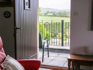 A room with a door leading to a balcony with a view of a vineyard and hills.