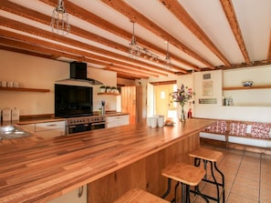 A kitchen with wooden beams, a large island with stools, a black stove, and a hanging light fixture. - The Old Farmhouse, Westhope (Craven Arms)