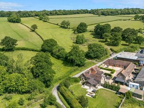 An aerial view of a rural property with fields, trees, and a large house with multiple buildings. - The Old Farmhouse, Westhope (Craven Arms)