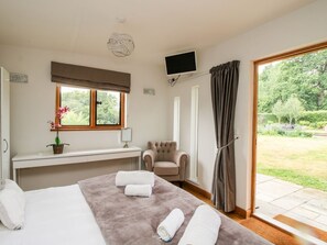 A hotel room with a bed, a desk, a chair, a TV, and a view of the garden. - The Old Farmhouse, Westhope (Craven Arms)