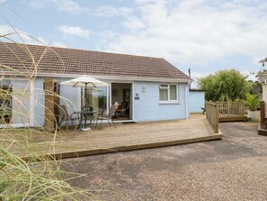 A single-story house with a wooden deck, a glass door entrance, and a small patio area with outdoor furniture. - Buddleia Cottage, Seaview (Seaview)