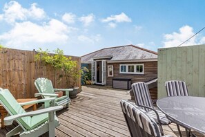 Eine Holzdar Terrasse mit Gartenmöbeln, ein Holzzaun und ein Haus mit Garage.