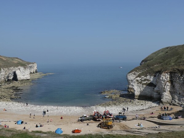 A coastal beach with tents, boats, and rocky cliffs.