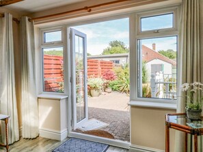 Ein Zimmer mit einer Tür, die in einen Garten führt, einem Fenster mit Gartensicht und einem kleinen Tisch mit einer Pflanze.