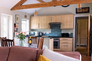 A kitchen with wooden cabinets, a dining table with chairs, and a vase with flowers. - Alwent Mill, Staindrop (Darlington)