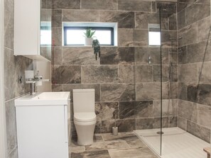 A bathroom with a toilet, sink, shower, and a window with a plant. - The Tyre Barn: A Unique Retreat (Whitchurch)
