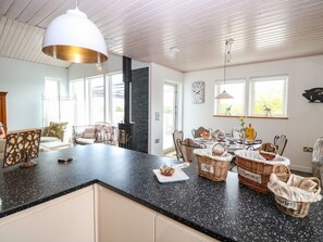 A kitchen with a black granite countertop, white cabinets, a hanging light fixture, and a dining area with wicker baskets. - Links View Retreat in Fritton (Great Yarmouth)