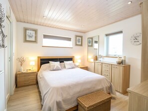 A bedroom with a bed, bedside tables, a dresser, a mirror, and a window. - Links View Retreat in Fritton (Great Yarmouth)
