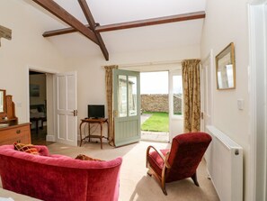 A room with a red sofa, a wooden chair, a television, and a door leading to a garden. - Sheep Pen Cottage, Durham (Durham)