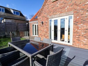Eine Terrasse mit Glastisch und Korbstühlen, ein Ziegelgebäude mit rotem Dach und eine Glastür.