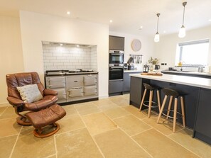 A modern kitchen with a central island, a dining area with bar stools, and a leather chair. - Cae Sam: Charming Retreat in Pentraeth (Pentraeth)