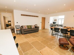 A spacious living area with a dining table, chairs, a sofa, and a kitchen in the background. - Cae Sam: Charming Retreat in Pentraeth (Pentraeth)