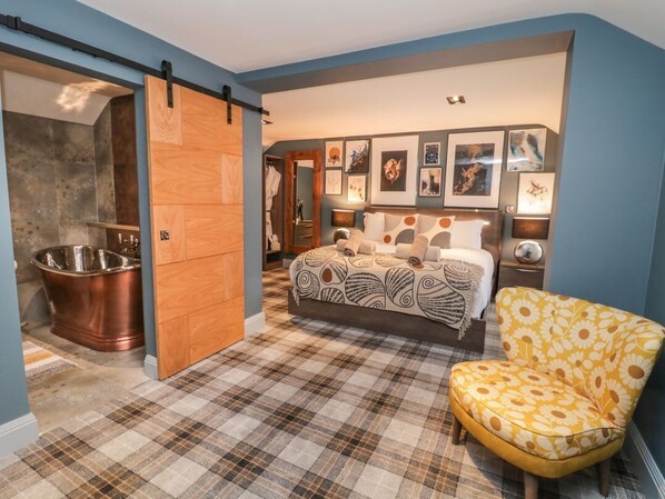 Un dormitorio con una cama, una silla, una puerta corredera y un muro con cuadros.