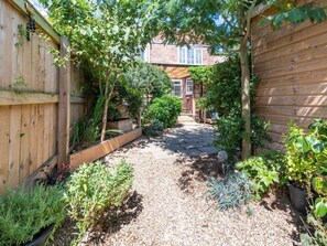 Ein Gartenweg führt zu einem Haus mit Ziegelaußenwand, umgeben von Holzzäunen und verschiedenen Pflanzen.