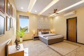 A modern bedroom with a bed, bedside tables, a ceiling fan, an air conditioning unit, and a window with a view. - Abhinandan Farm by ELIVAAS (Amer)