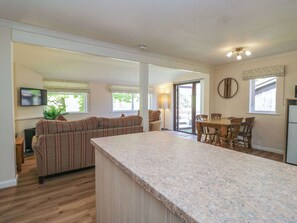 A modern kitchen with a granite countertop, a dining area with wooden chairs, a sofa, and a television.