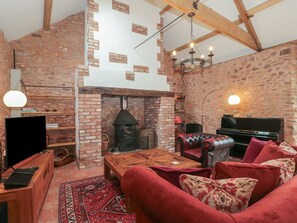 Una sala de estar acogedora con chimenea, televisor, piano y muebles tapizados en rojo.