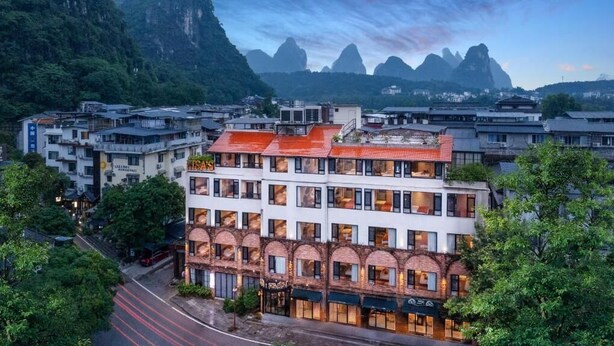 A multi-story hotel with a red roof, large windows, and a view of mountains. - Yangshuo Lisa Boutique Hotel (Guilin)