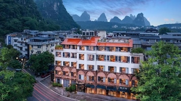 A multi-story hotel with a red roof, large windows, and a view of mountains.