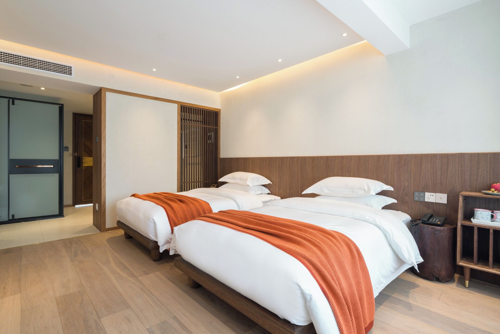 Ein Hotelzimmer mit zwei Betten, einem Holz-Kopfbrett, einem Nachttisch und einer kleinen Ablagefläche mit Telefon und Tasse.