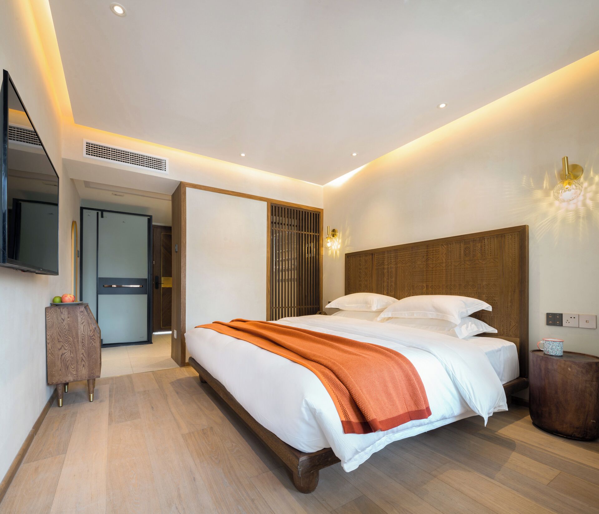Ein modernes Hotelzimmer mit einem großen Bett, einem hölzernen Kopfteil, einem Nachttisch, einem Spiegel und einer Wandleuchte.