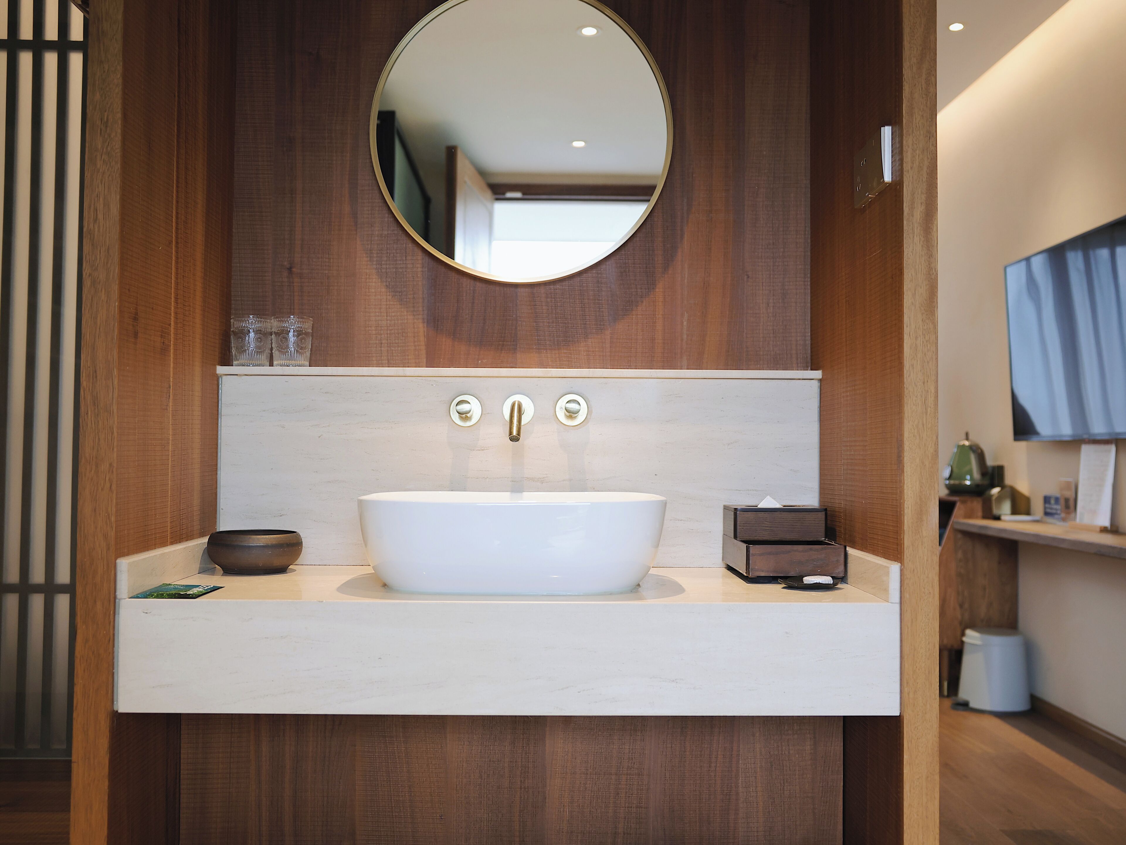 Une salle de bain avec un lavabo blanc, un miroir rond et un meuble-lavabo en bois.