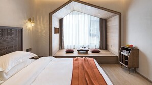 A bedroom with a large bed, a window seat with cushions, a bedside table, and a small wooden cabinet. - Yangshuo Lisa Boutique Hotel (Guilin)