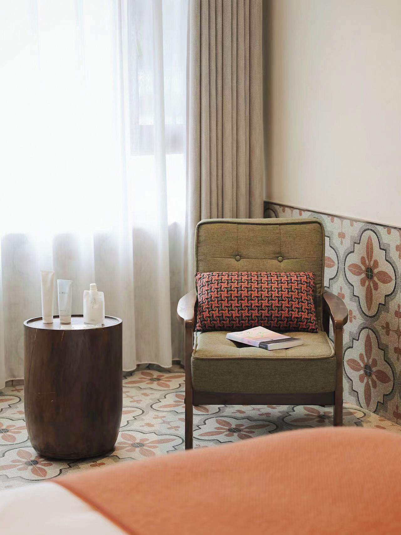 A hotel room with a chair, a small table with toiletries, and a patterned wall.
