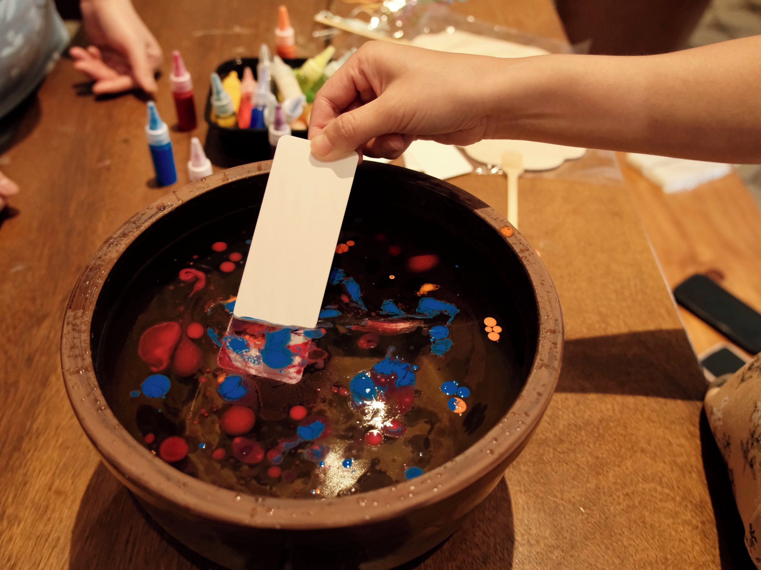 A person holding a card over a bowl with colorful paint splatters.