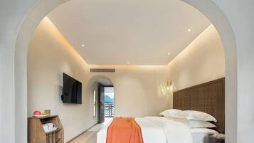 A modern hotel room with a bed, a TV mounted on the wall, a wooden side table with a cup and a book, and a view through an arched doorway.