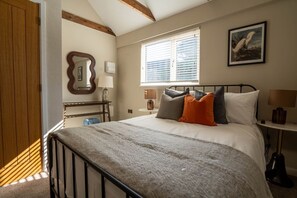 Ein Schlafzimmer mit Bett, Nachttischlampen, einem Fenster mit Jalousien, einer Holztür und einem gerahmten Bild an der Wand.