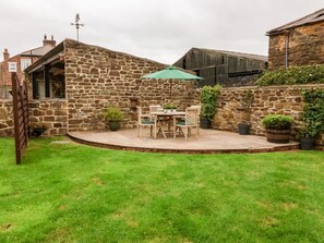Un bâtiment en pierre doté d’un patio comprenant une table et des chaises, le tout entouré d’une pelouse bien entretenue.