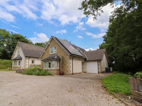 A two-story house with a gravel driveway, a garage, and a garden area with plants.